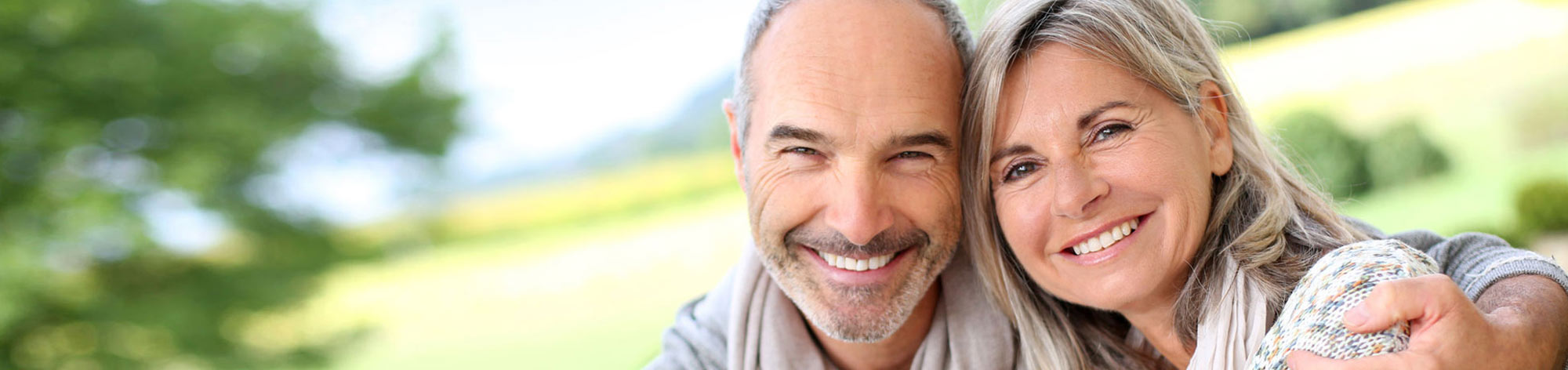 גבר ואשה מתחבקים ומחייכים על רקע של עצים ירוקים